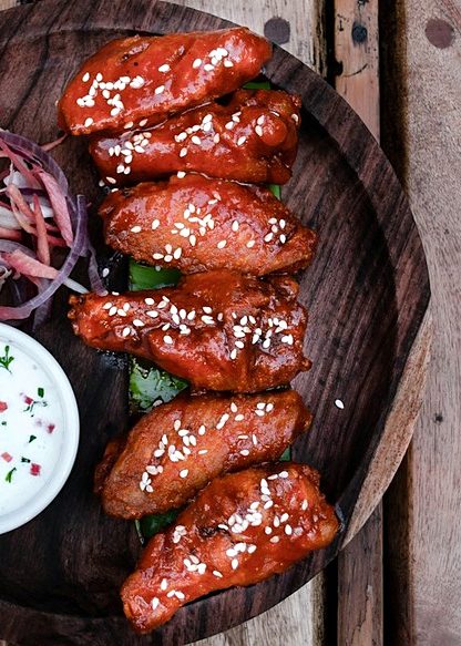Glazed grilled links sprinkled with sesame seeds on a dark wooden platter with a dipping sauce